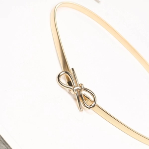 Detailed close-up of golden metal spring belt with a delicate bow buckle decoration