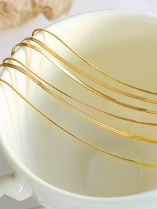 Close-up of dual-layer gold snake and blade chains draped over white ceramic decor