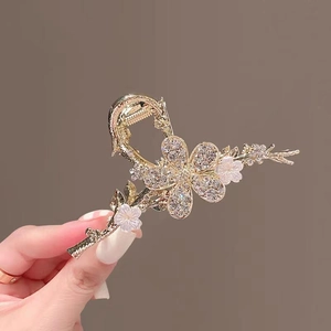 Close-up of golden metal flower hair claw clip with rhinestones and white petals