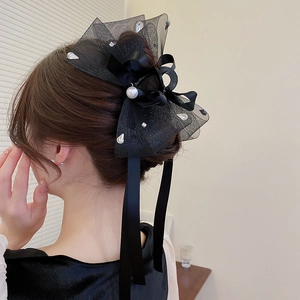 Détail d'une pince à cheveux avec nœud en dentelle noire, perles et longs rubans