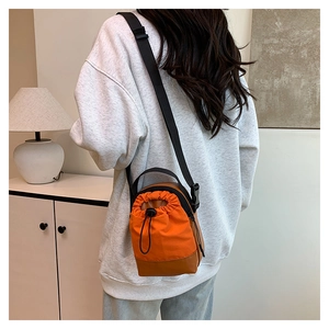 Back view of a model wearing a casual orange canvas drawstring crossbody bag with leather trim