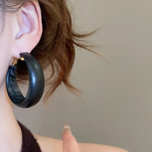 Close-up of black leather hoop earrings with fine stitching and golden metal clasp