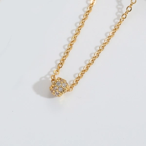 Detailed view of a gold cylindrical pendant necklace set with shimmering white zircons
