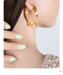 Close-up of a model wearing gold twisted U-shaped earrings with a polished finish