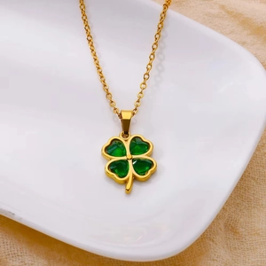 Detailed close-up of a golden four-leaf clover pendant with green heart-shaped gemstones