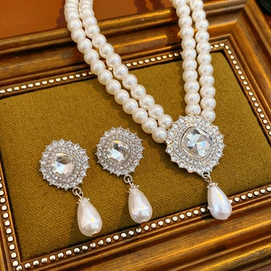 Close-up of double-layer pearl necklace and teardrop earrings on green velvet pad