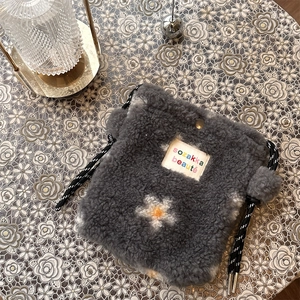 Close-up of dark grey plush crossbody bag with flower patterns and woven drawstring