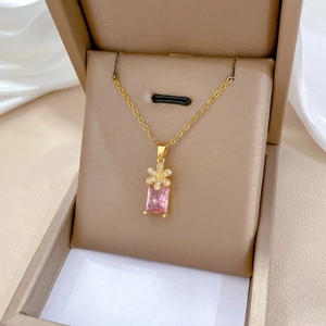 Macro shot of gold necklace featuring micro-set flower and rectangular pink gemstone