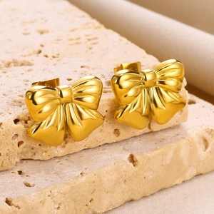 Detail showing high-quality gold bow earrings with a matte texture on a stone background