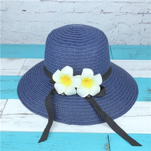 Detail of navy straw sun hat featuring decorative white plumeria flowers and a black ribbon bow
