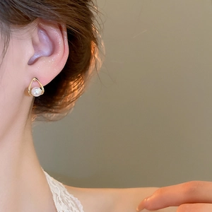 Close-up of minimalist gold teardrop stud earring with a white pearl on a model