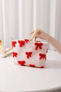 Detail of pink knitted makeup pouch with red pompom bow and woven brand tag