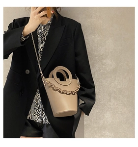 Detail of khaki bucket bag with circular handle and chain accessory on a model
