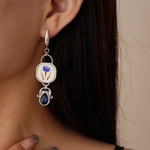 Gros plan sur boucle d'oreille asymétrique avec motif tulipe mauve et zircon bleu