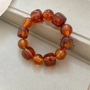 Détail macro du bracelet en résine ambrée avec perles carrées et rondes sur base blanche