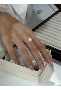 Dettaglio di un anello con perla bianca e fascia d'argento su scatola beige per gioielli