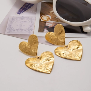 Detailed view of gold heart stud earrings with radial texture on a stylish lifestyle background