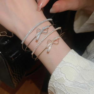 Close-up of stacked gold and silver bangles with zircon bows worn on a wrist