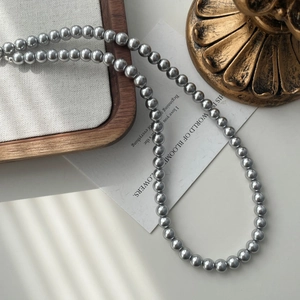 Detail shot of long grey faux pearl necklace with metallic luster on white background