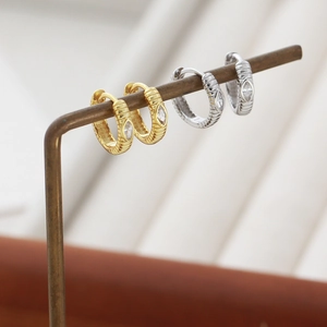 Detail of gold and silver textured hoop earrings with marquise-cut zircon stones