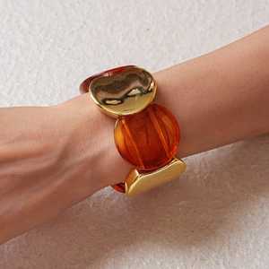 Dettaglio del bracciale elastico largo con metallo dorato fluido e resina ambrata