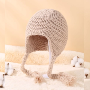 Detailed knit texture of a beige earflap hat with decorative braided tassels and soft lining