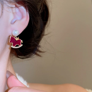 Close-up of red velvet pony earring with gold trim and pearl detail on female model