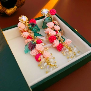 Détail de boucles d'oreilles fleurs en cristal rose avec feuille verte et frange dorée