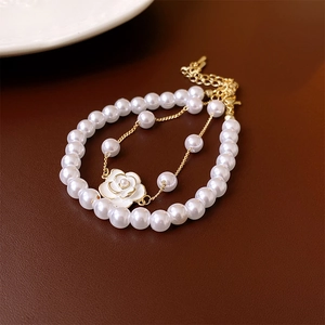 Close-up of double-layer bracelet featuring white camellia pendant and pearls on gold chain