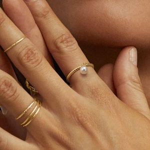 Nahaufnahme eines gedrehten S925 Silberrings in Gold mit Süßwasserperle am Finger getragen