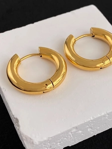 Polished thick gold hoop earrings on a white stone base with a sharp mirror finish