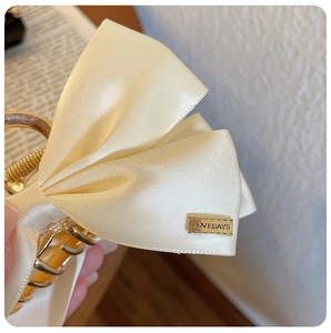 Detail of cream satin bow hair claw clip with golden metal hardware and LOVEDAYS plate