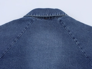 Detail of double-stitched collar and raglan sleeve seams on blue denim cape jacket