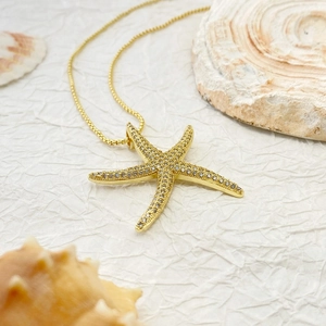 Detailed view of a gold starfish necklace with shimmering pavé crystals on a seashell background