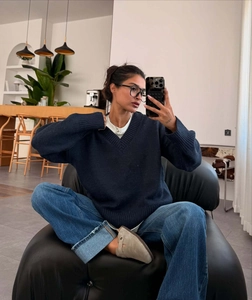 Navy V-neck knit sweater styled with blue jeans and gray suede mules in a chic interior