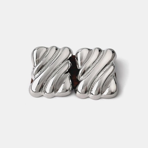 Close-up of polished silver wavy geometric earrings on dark wood and white background