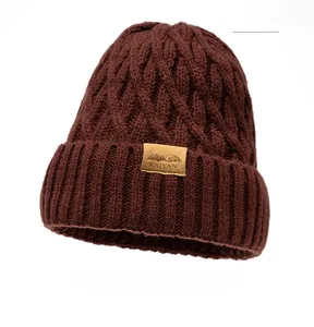 Macro detail of wine red beanie showing thick cable knit texture and leather logo patch