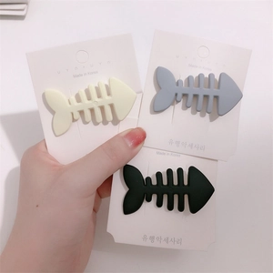 Three fishbone-shaped hair clips in cream, blue-gray, and black on a card