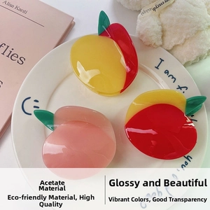 Detail of cute fruit-shaped acetate hair claws in pink, red, and yellow on a white dish