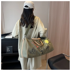 Army green canvas travel bag with graffiti prints shown worn over a beige trench coat