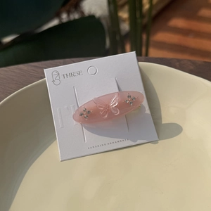 Pink oval acetate hair clip with crystal butterfly decoration on a display card