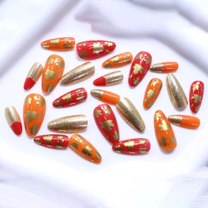 Autumn almond press-on nails featuring red and orange maple leaf patterns with gold glitter