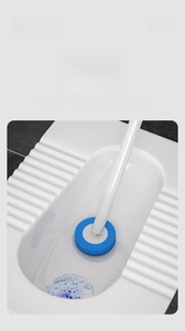 Close-up of disposable toilet brush cleaning a ceramic squat toilet with long white handle