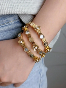 Detailed view of three-piece gold stretch bracelets with smile, flower and heart charms