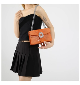 Model wearing orange croc-embossed crossbody bag with crystal buckle and chain strap