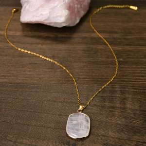 Macro shot of rectangular pink crystal pendant with gold plating on wood background