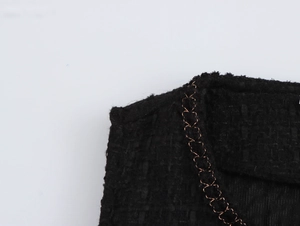 Dettaglio di abito in tweed nero con catena dorata e trama intrecciata raffinata