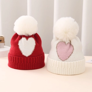Detail of baby knit hats with heart patterns, faux fur pom-poms and ribbed earflaps