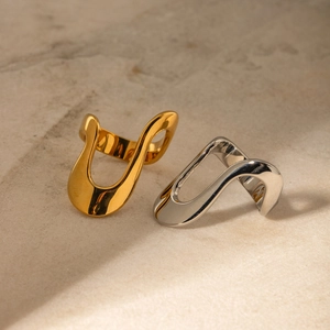 Close-up of irregular S-shaped gold and silver rings on a beige stone surface