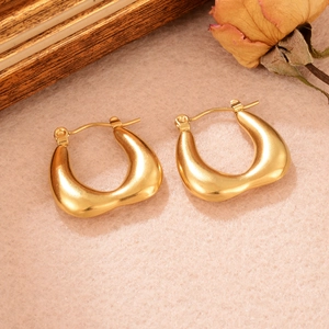 Détail de grandes boucles d'oreilles en métal doré torsadé sur une surface en velours